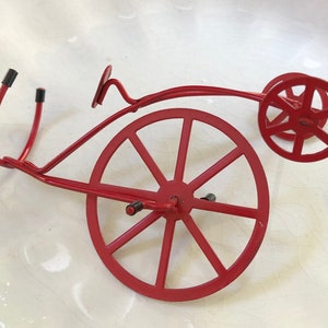 May include: A red metal bicycle sculpture with two wheels. The sculpture is made of thin metal and has a simple design.