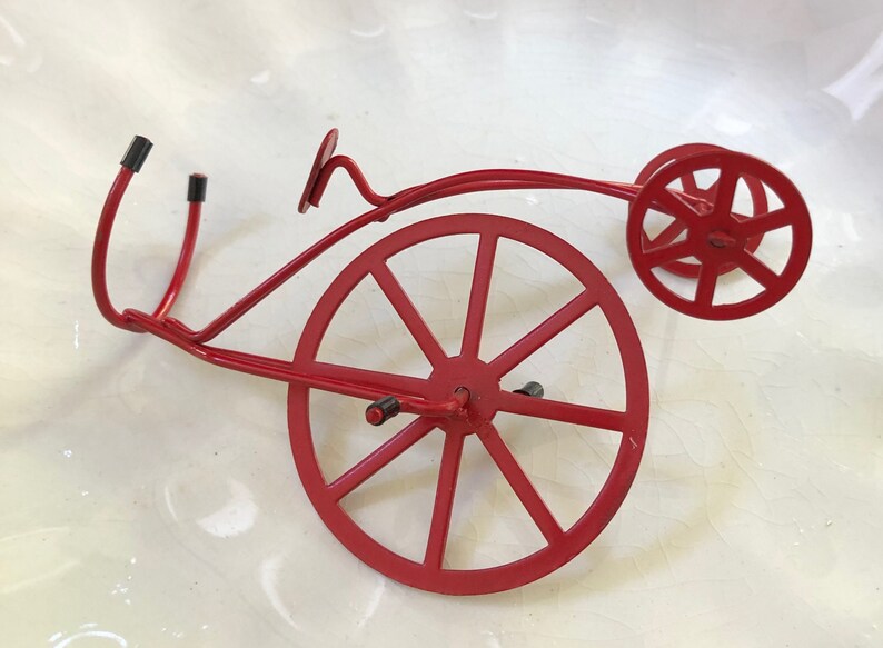 May include: A red metal bicycle sculpture with two wheels. The sculpture is made of thin metal and has a simple design.