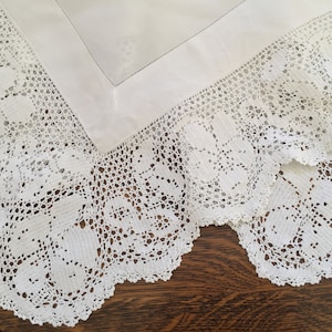 May include: White crocheted tablecloth with a delicate floral pattern. The tablecloth has a scalloped edge and is made of fine, intricate lace.
