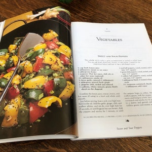 May include: A recipe for Sweet and Sour Peppers, featuring a close-up of the finished dish with red, green, and yellow bell peppers, scallions, and sesame seeds. The recipe includes ingredients like lemon juice, tamari, honey, and chili oil.
