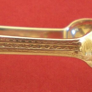 May include: A pair of silver sugar tongs with a decorative design. The tongs are made of metal and have a polished finish.
