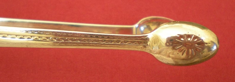 May include: A pair of silver sugar tongs with a decorative design. The tongs are made of metal and have a polished finish.