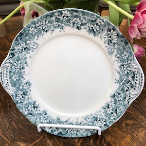 Puede incluir: Un plato de servir de cerámica blanca con un diseño floral azul alrededor del borde. El plato tiene dos asas a los lados.