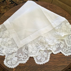 May include: White linen tablecloth with a delicate crocheted lace border. The lace features a floral design.
