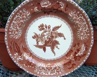 May include: A brown and white ceramic plate with a floral design. The plate has a raised rim and a scalloped edge.