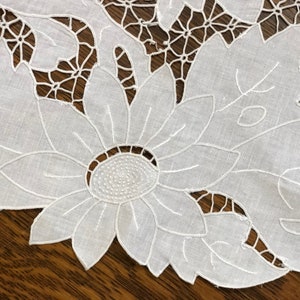May include: White cotton lace tablecloth with a delicate floral design featuring a large sunflower in the center.