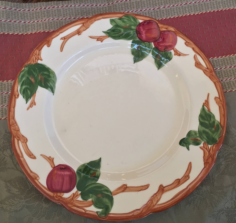 Pu&ograve; includere: Un piatto in ceramica bianca con un design a ramo marrone e illustrazioni di mele rosse e verdi.
