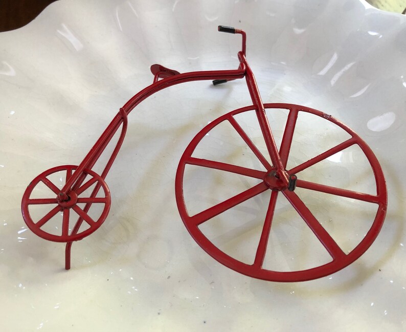 May include: A red metal toy bicycle with a large front wheel and a smaller back wheel. The bicycle is made of thin metal and has a simple design.