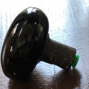 May include: A black ceramic door knob with a green plastic base.