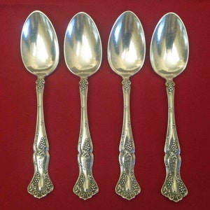May include: Set of four silver spoons with ornate handles featuring a grapevine design. The spoons have a polished finish and are in excellent condition.