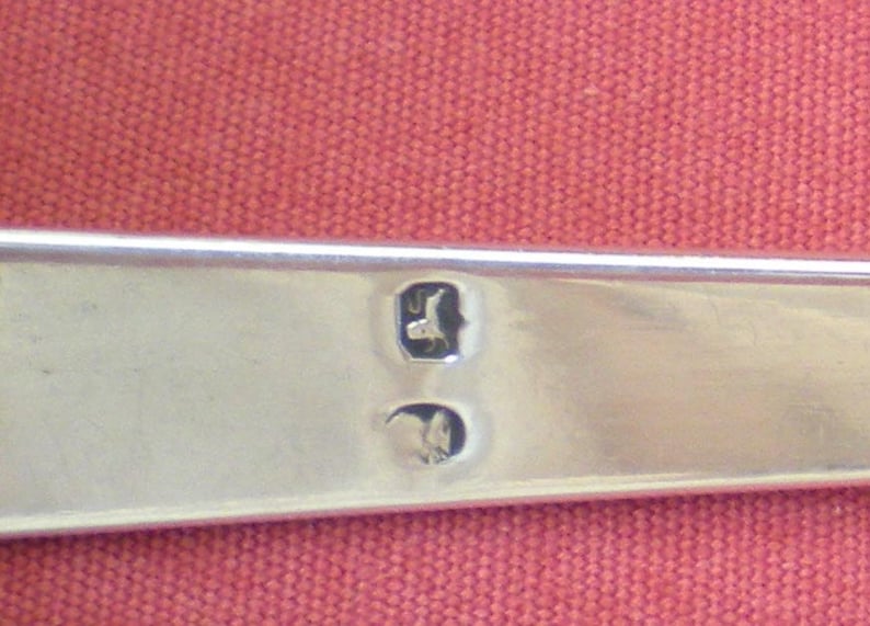 May include: Close-up of a silver object with two hallmarks. The hallmarks are in the shape of a bird and a crown.