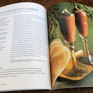 May include: Two glasses of chocolate mousse with orange zest on top, served on a gold tray with two silver spoons. The mousse is a rich, dark brown color and the glasses are tall and elegant.