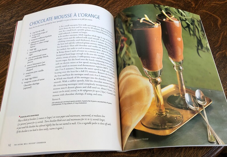May include: Two glasses of chocolate mousse with orange zest on top, served on a gold tray with two silver spoons. The mousse is a rich, dark brown color and the glasses are tall and elegant.