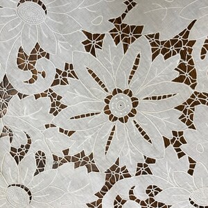 May include: White cotton lace tablecloth with a delicate floral design. The tablecloth features intricate cutouts and embroidery, creating a beautiful and elegant pattern.