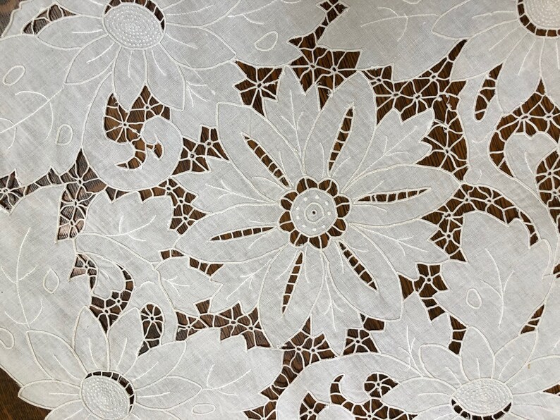 May include: White cotton lace tablecloth with a delicate floral design. The tablecloth features intricate cutouts and embroidery, creating a beautiful and elegant pattern.