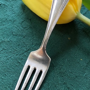 May include: A silver fork with an ornate handle, resting on a green tablecloth with a yellow tulip behind it.