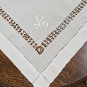 May include: White linen tablecloth with a delicate lace border and an embroidered letter "L" in the center.