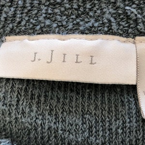 May include: A white tag with the text "J.Jill" and a white tag with the text "M 85% Cotton 15% Polyester Made in U.S.A. RN 97641" on a dark gray fabric.