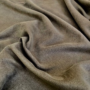May include: Close-up of a soft, dark brown fleece fabric with a textured surface. The fabric is folded and draped, creating a smooth, flowing look.