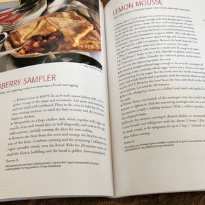 May include: A cookbook page with a recipe for Pear-Cranberry Sampler, a warm fruit dessert with a French toast topping. The recipe includes ingredients like pears, cranberries, corn starch, sugar, and bread. The image also shows a close-up of the dessert, which is baked in a square baking dish.