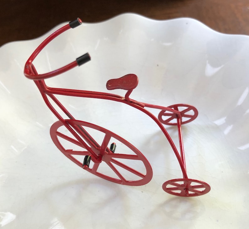 May include: A red metal toy bicycle with a single large front wheel and two smaller back wheels. The bicycle has a curved handlebar and a small seat.
