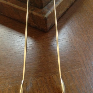 May include: Silver sugar tongs with rounded ends. The tongs are lying on a wooden surface.