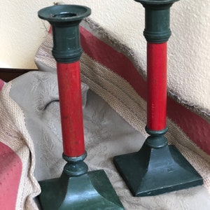 May include: A pair of green metal candle holders with red wooden stems. The candle holders have a square base and a round top.