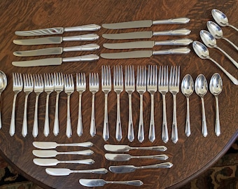May include: A set of silverware, including forks, knives, and spoons, laid out on a wooden table. The silverware is made of polished silver and has a traditional design.