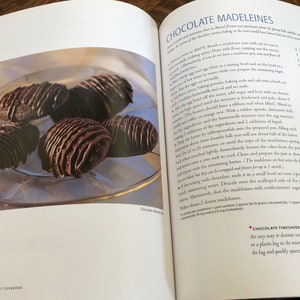 May include: A close-up of a plate of chocolate madeleines, a type of French pastry. The madeleines are topped with a chocolate drizzle and are arranged in a circular pattern on the plate.