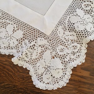 May include: White crocheted tablecloth with a delicate floral pattern. The tablecloth has a scalloped edge and is made of fine, intricate lace.
