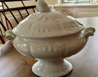 May include: White porcelain serving dish with a lid. The dish has a decorative floral design and a pedestal base.