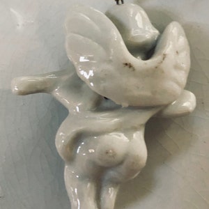 May include: White porcelain angel ornament with wings outstretched, hanging from a gold string.