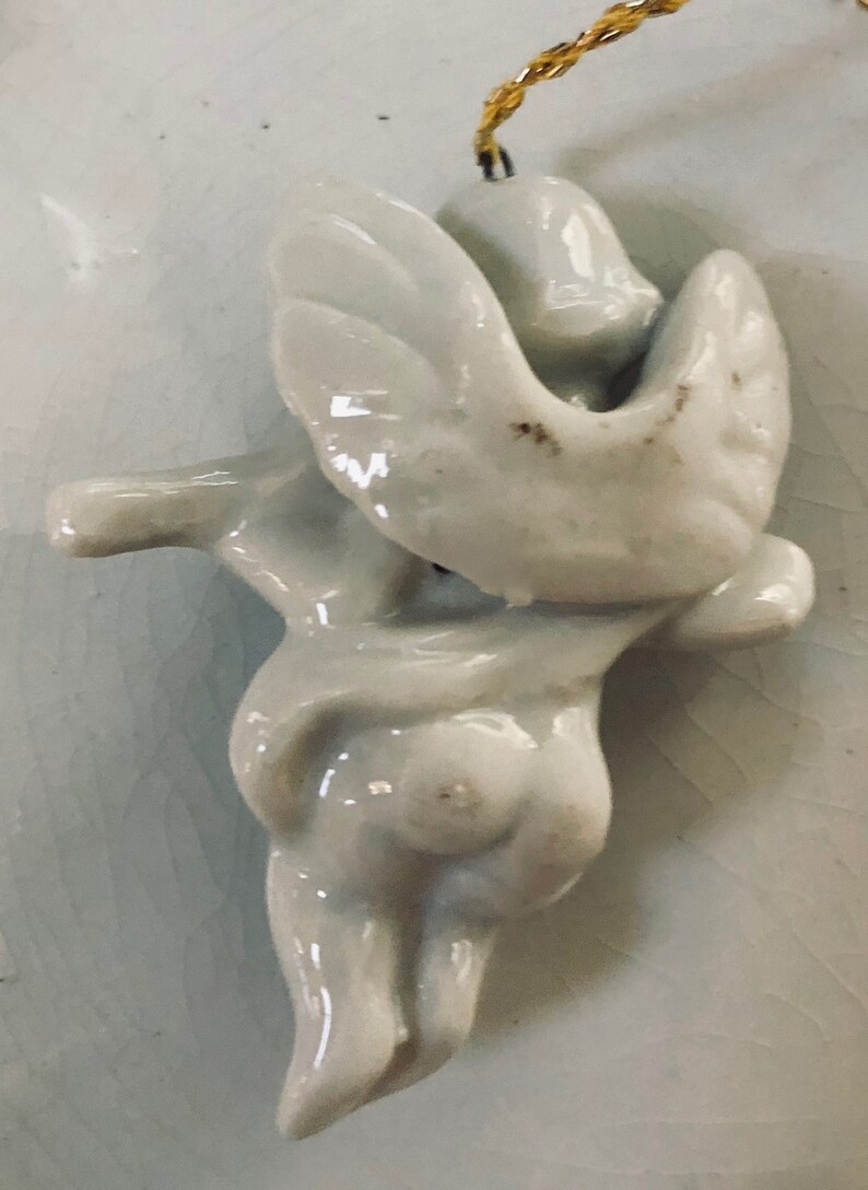 May include: White porcelain angel ornament with wings outstretched, hanging from a gold string.