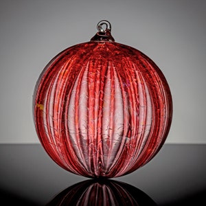 May include: A red glass Christmas ornament with a textured, ribbed surface. The ornament is round and has a silver loop at the top.