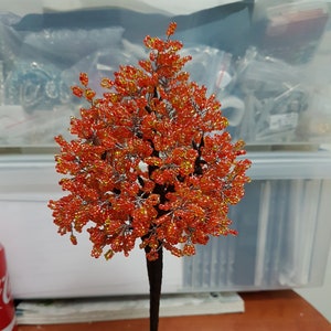 Peut inclure: Un arbre en perles avec des perles orange et jaunes, sur une tige de fil noir, avec un support en métal.