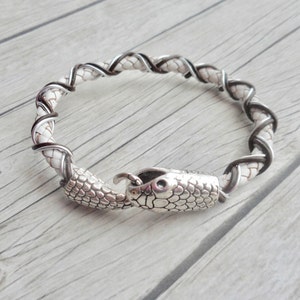 Op de afbeelding: Een wit en zwart gevlochten leren armband met een zilveren slangenkoppenvormige sluiting.