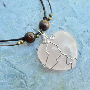 May include: A pink rose quartz heart pendant necklace with a silver wire wrap, brown wooden beads, and a brown leather cord.