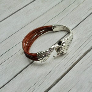 Peut inclure: Un bracelet en cuir marron avec un fermoir en forme de tête de serpent argenté.