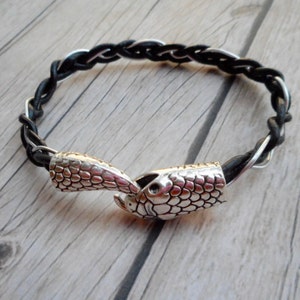 May include: A black leather bracelet with a silver snake clasp. The bracelet is braided and has a textured finish.