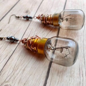 May include: A pair of earrings featuring small light bulbs wrapped in copper wire and accented with gray beads.