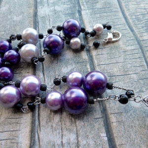 Peut inclure: Un collier en cha&icirc;ne argent&eacute;e avec des perles de couleur violette et blanche et des perles noires. Le collier a un fermoir argent&eacute; et un pendentif argent&eacute; avec un motif g&eacute;om&eacute;trique.