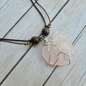 May include: A pink rose quartz pendant necklace with a wire wrapped design. The necklace is made with brown wooden beads and a brown leather cord.