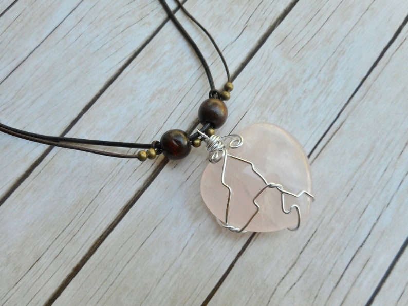 May include: A pink rose quartz pendant necklace with a wire wrapped design. The necklace is made with brown wooden beads and a brown leather cord.