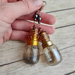 May include: A pair of dangle earrings featuring light bulb pendants wrapped in copper wire and accented with black beads. The earrings have a steampunk aesthetic.