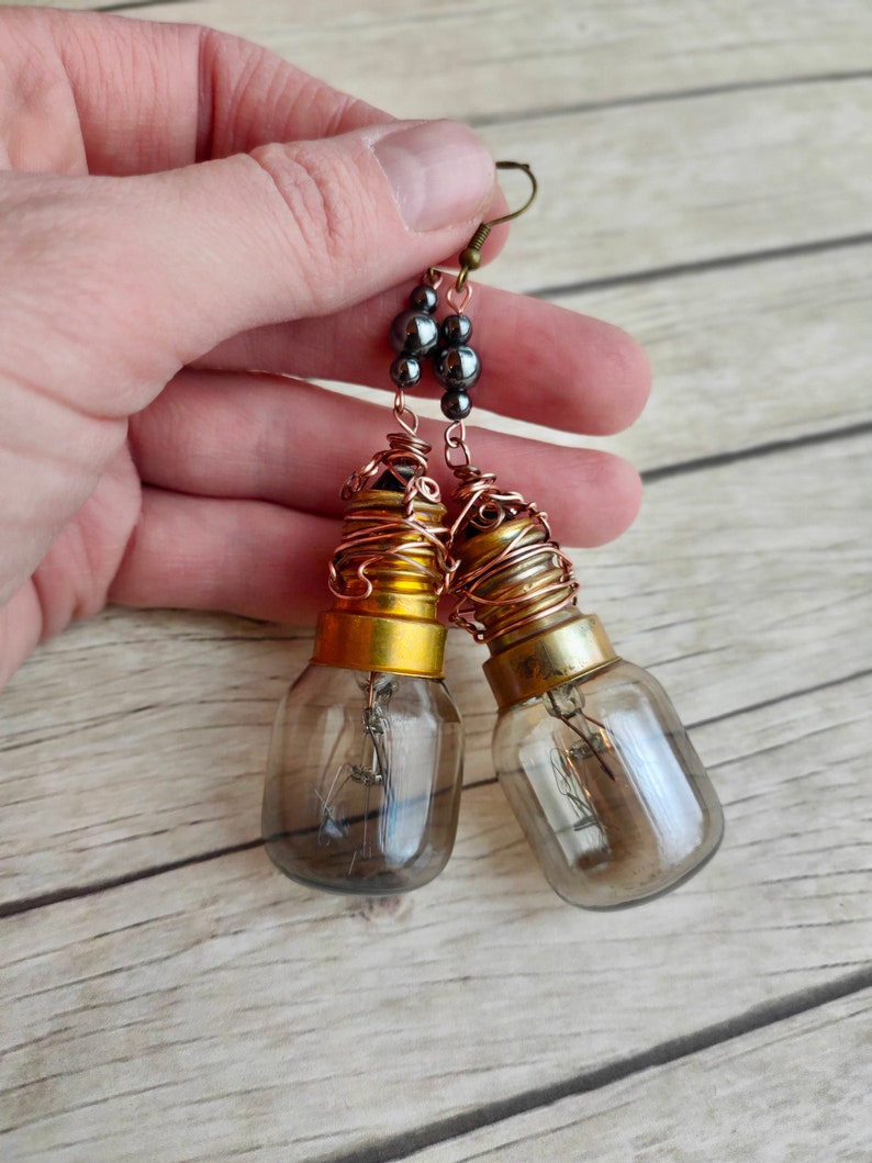 May include: A pair of dangle earrings featuring light bulb pendants wrapped in copper wire and accented with black beads. The earrings have a steampunk aesthetic.
