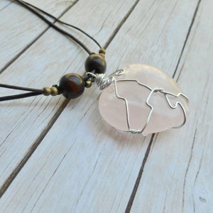 May include: A pink rose quartz heart pendant wrapped in silver wire, hanging from a brown leather cord with wooden beads.