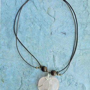 May include: A pink heart-shaped pendant necklace with a wire wrapped design. The necklace is made with brown leather cord and wooden beads.