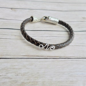May include: A brown leather bracelet with a silver clasp and a silver wire accent.
