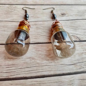 May include: A pair of earrings made from light bulbs with copper wire wrapped around the base and a dark gray bead at the top of each earring.