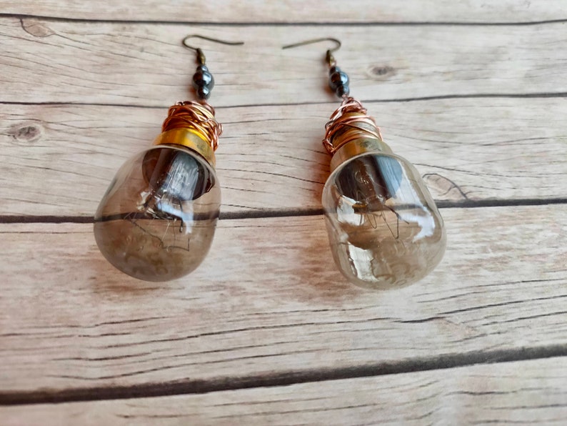 May include: A pair of earrings made from light bulbs with copper wire wrapped around the base and a dark gray bead at the top of each earring.